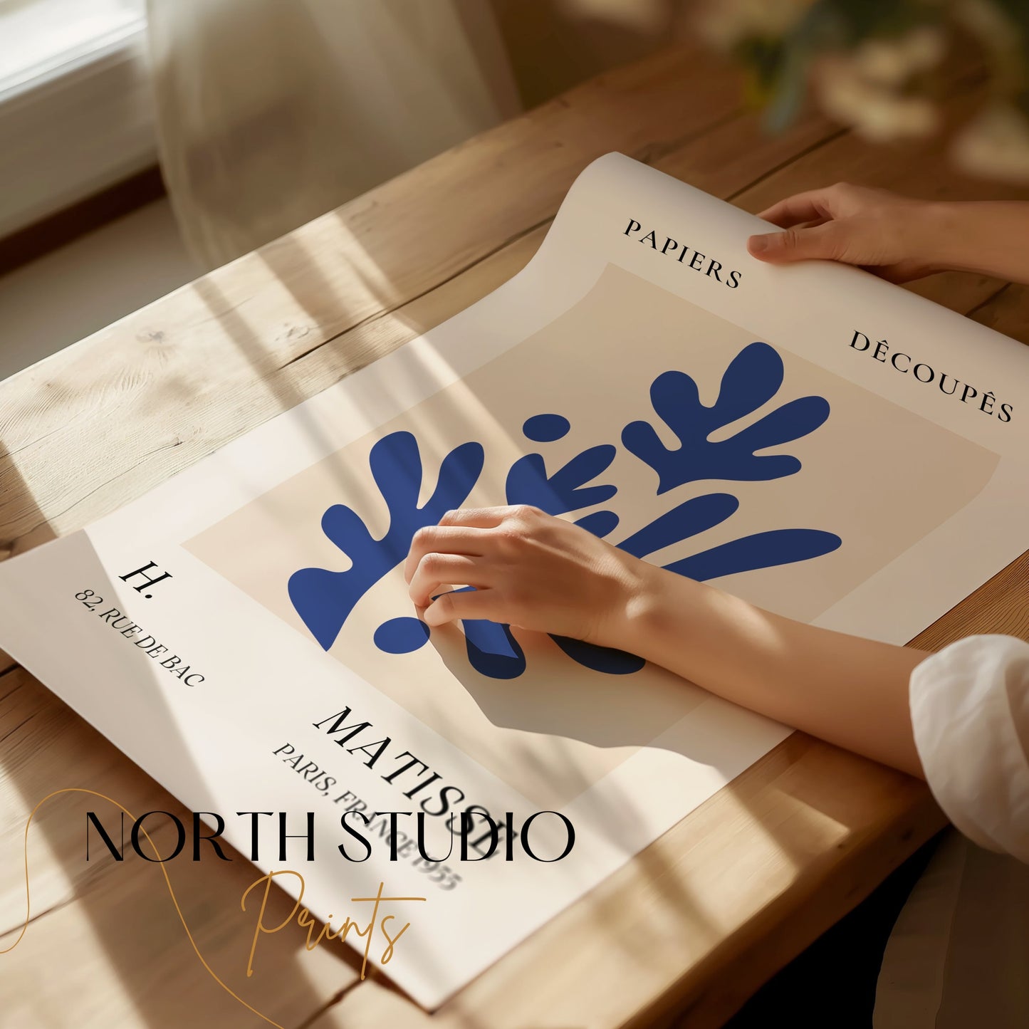 Unframed Matisse-style Parisian art print with blue botanical shapes, being handled on a wooden table, showcasing premium quality.