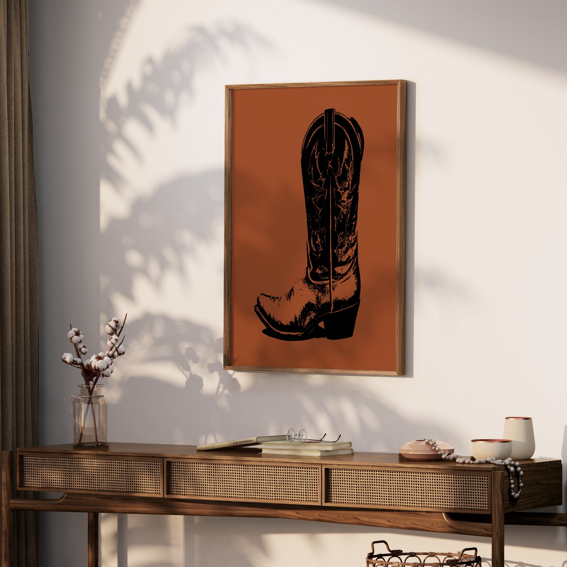 Framed black cowboy boot art on orange background above a wooden console table.