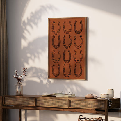 Framed artwork with twelve decorative horseshoes on a terracotta background.