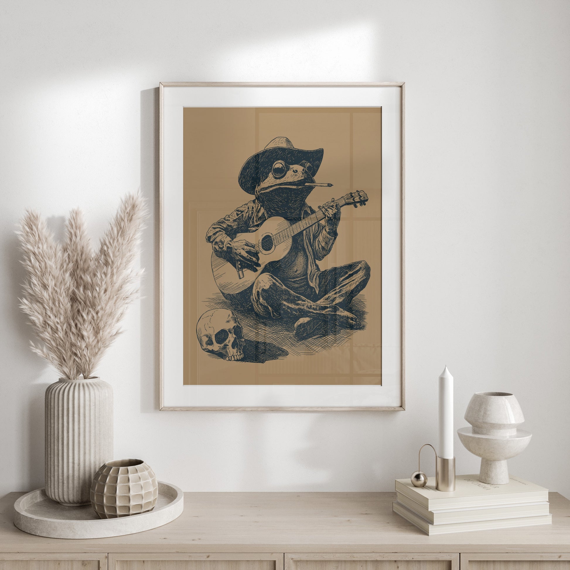 Framed artwork of a frog wearing a cowboy hat playing guitar beside a skull.