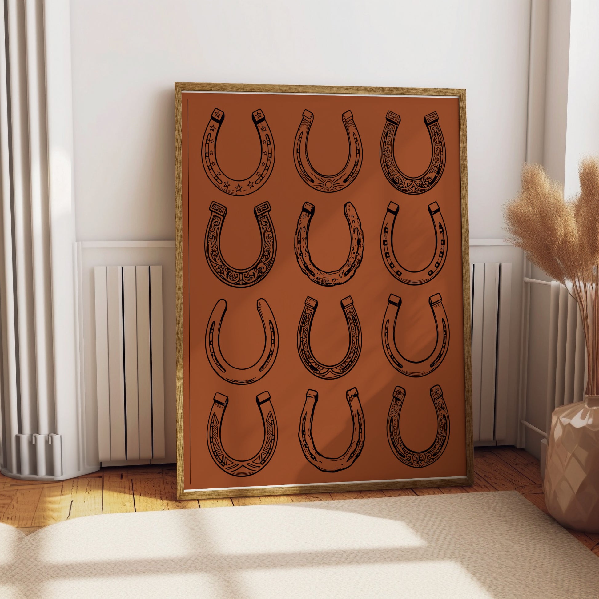 Framed artwork featuring twelve decorative horseshoes on a terracotta background.