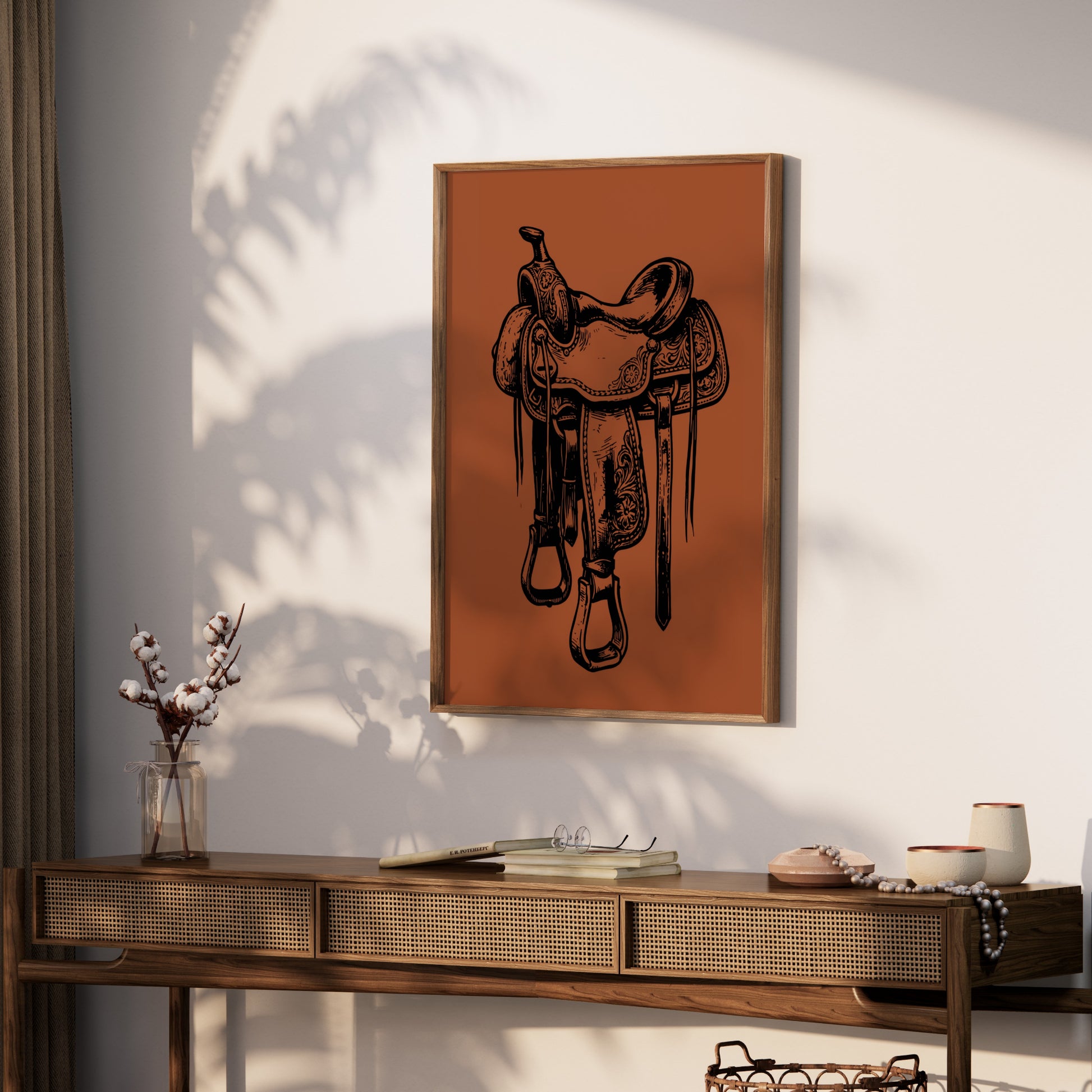 Framed black and white saddle illustration on an orange background hangs above a wooden console table.