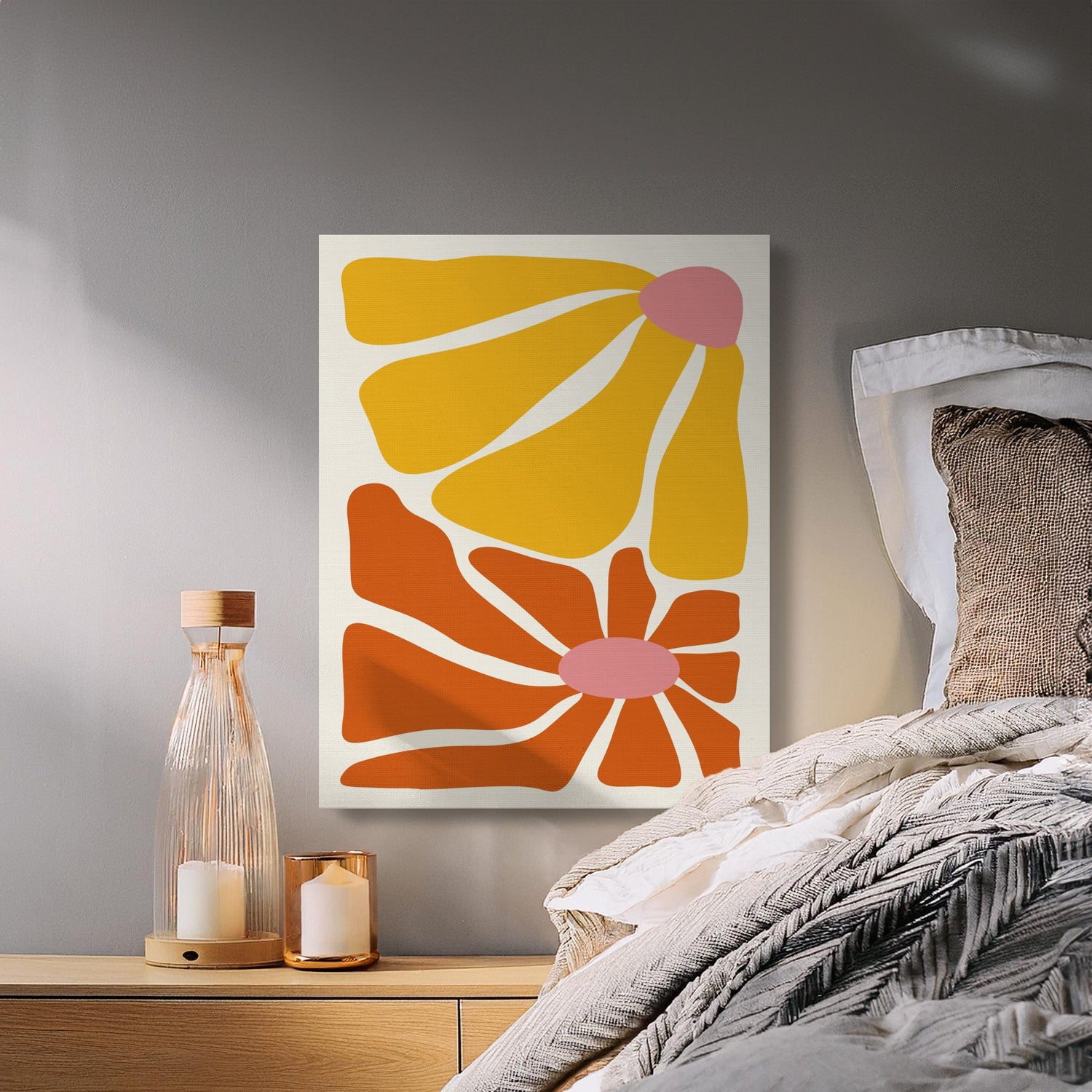 A bedroom features a wooden nightstand with a glass bottle, candles, and a bed. An abstract artwork with yellow and orange shapes on a white background hangs on the wall.