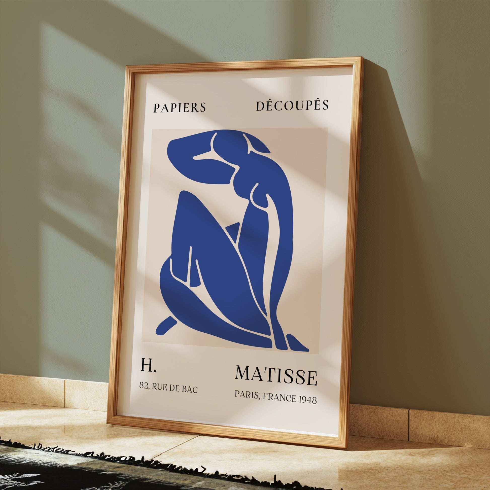 Abstract Blue Figure Henri Matisse art print in a gold frame, placed on a tiled floor with sunlight streaming in, ideal for minimalist decor.