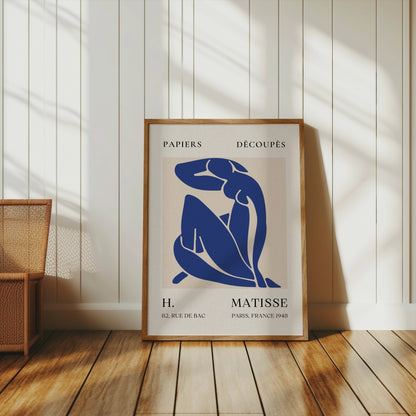 Abstract Blue Figure Henri Matisse art poster in a wooden frame, leaning against a white paneled wall with warm natural light, perfect for classic decor.