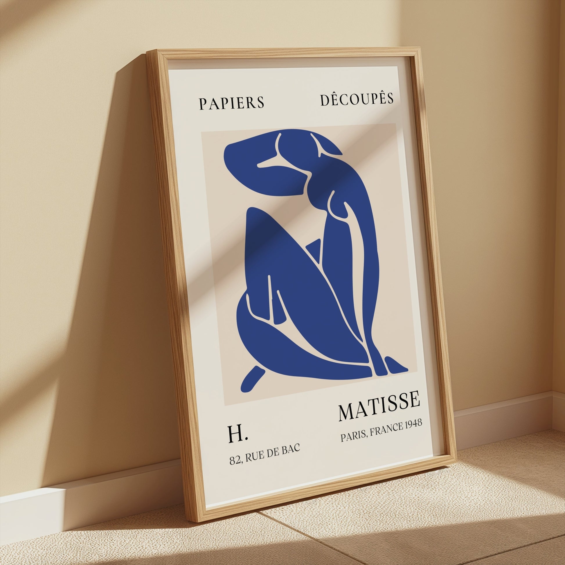 Abstract Blue Figure Henri Matisse art print in a light wooden frame, leaning against a beige wall with soft sunlight, ideal for modern wall decor.