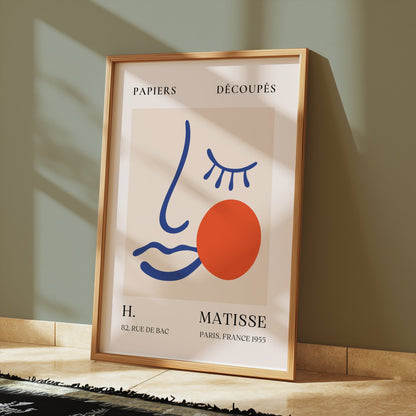 Artistic Matisse Papercut Face Design Wall Art Poster in a wooden frame, styled on a tiled floor with shadows from natural light for a modern aesthetic.