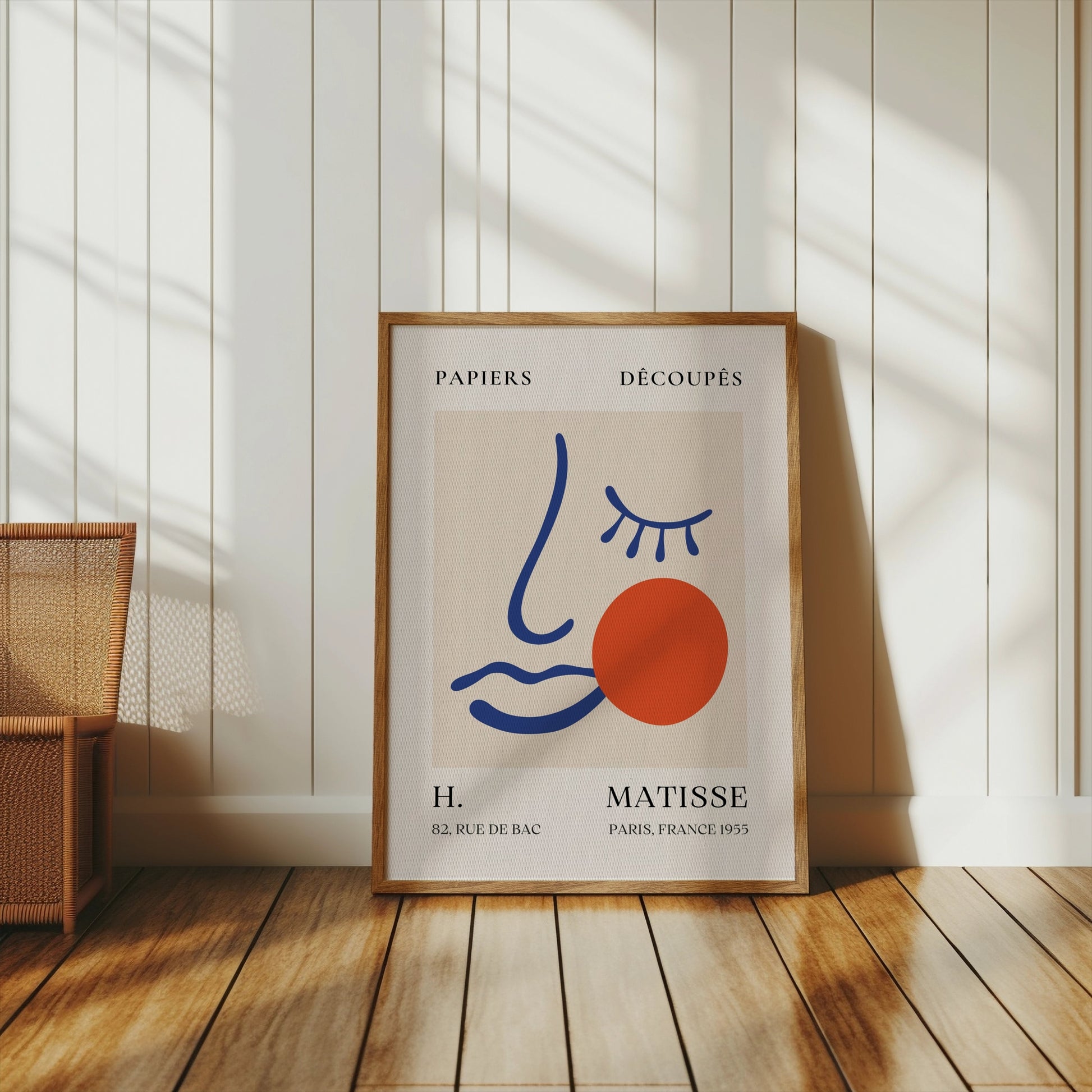 Artistic Matisse Papercut Face Design Wall Art Poster in a wooden frame, placed on a wooden floor in a bright room with white panel walls and natural light.