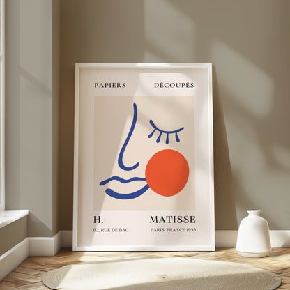 Artistic Matisse Papercut Face Design Wall Art Poster in a white frame, leaning against a neutral wall in a bright, minimalistic interior setting.