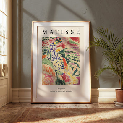 Framed Matisse La Japonaise poster placed on the floor near a window with soft sunlight. Vibrant colors enhance the room's ambiance.