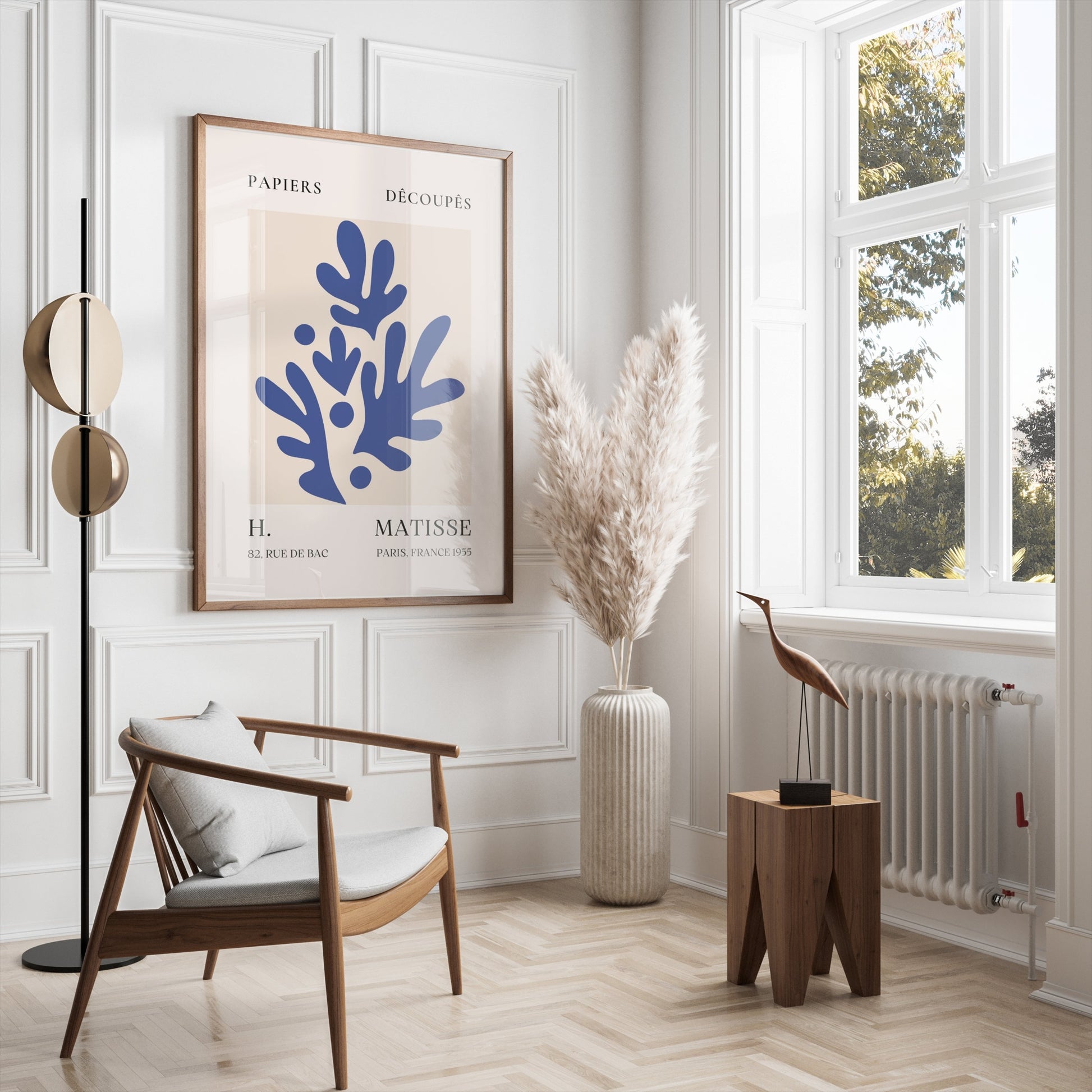 Matisse-inspired abstract art poster with blue leaf cut-outs, framed and styled in a bright, modern living room with neutral tones.