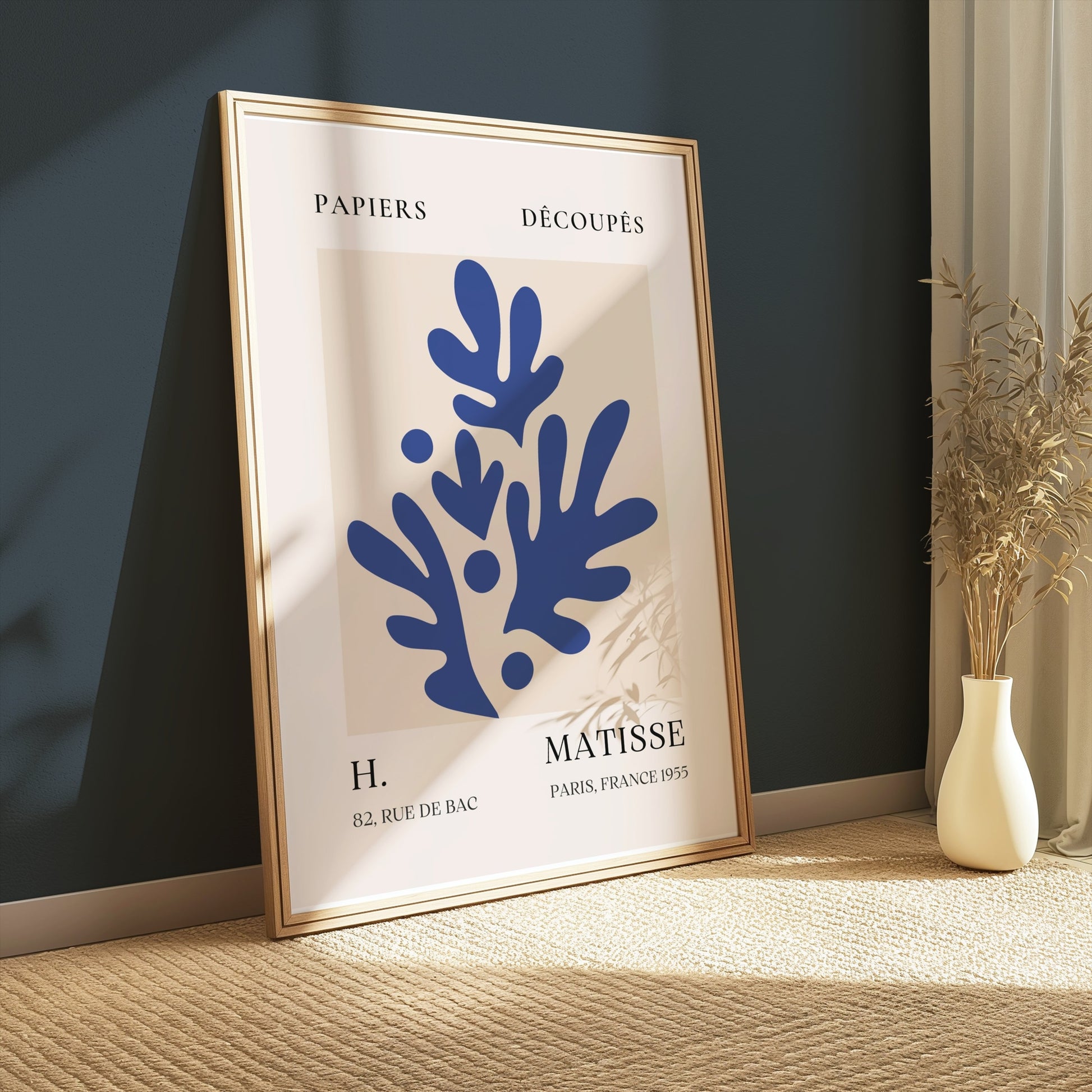 Framed Matisse-inspired poster featuring blue leaf cut-outs, leaning against a dark green wall with soft natural lighting.