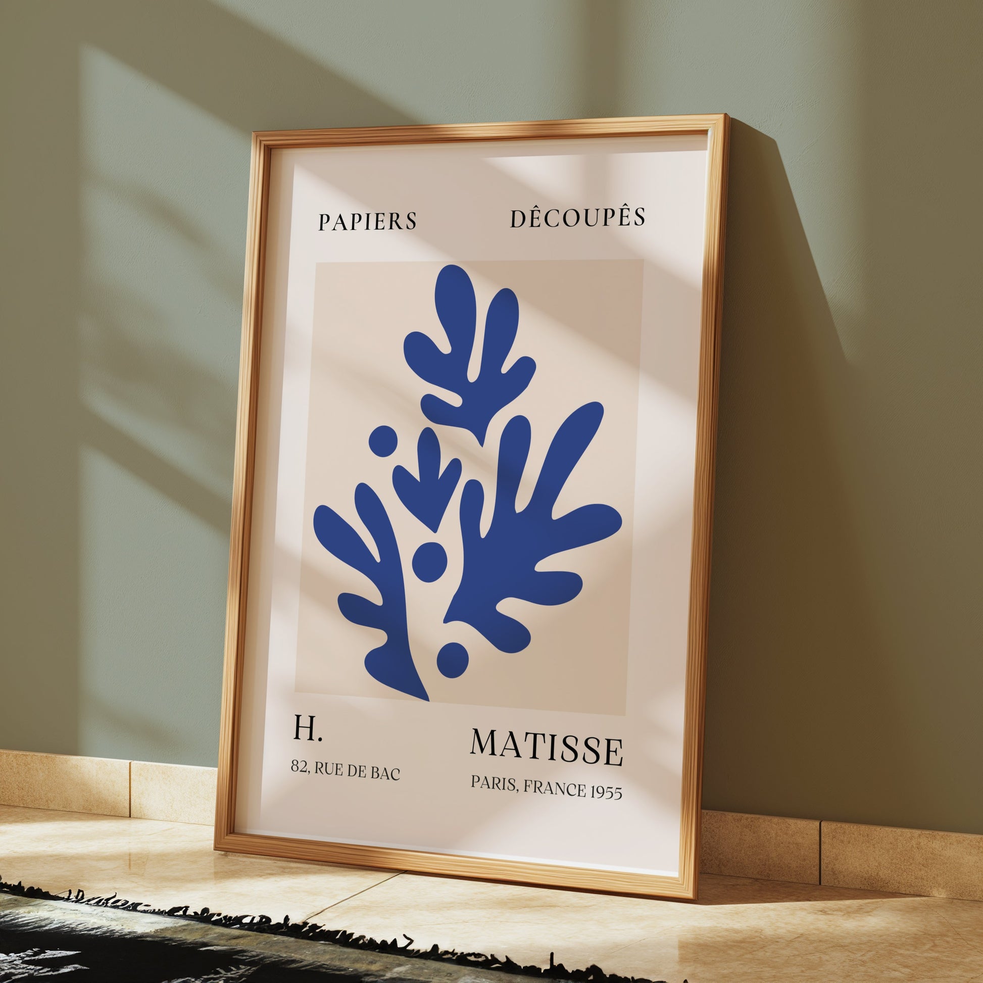 Framed Matisse-style Parisian art print with blue abstract botanical design, leaning against a green wall, perfect for stylish interiors.