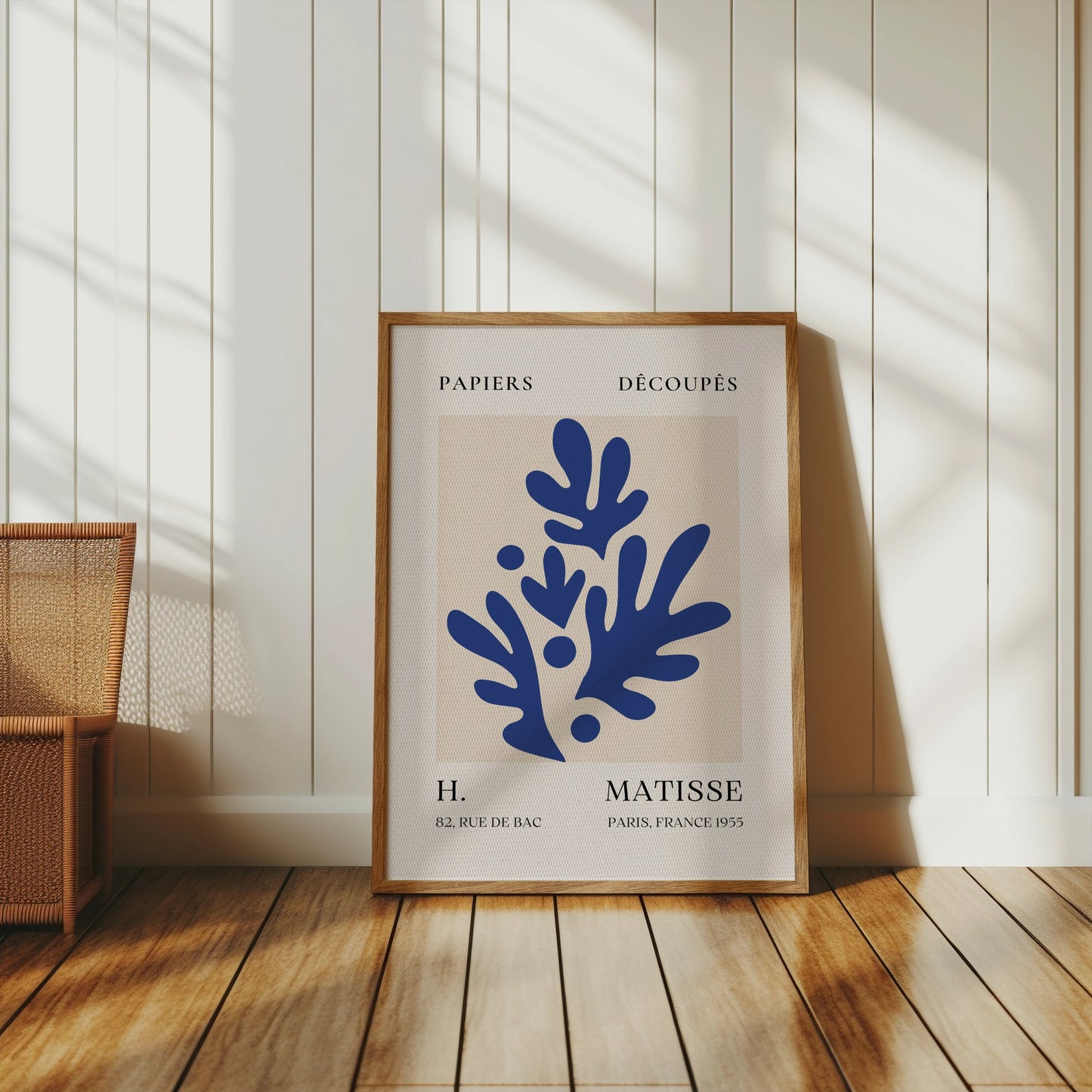 Blue botanical Matisse-style Parisian art print in a wooden frame, leaning against a white paneled wall, ideal for minimalist home decor.