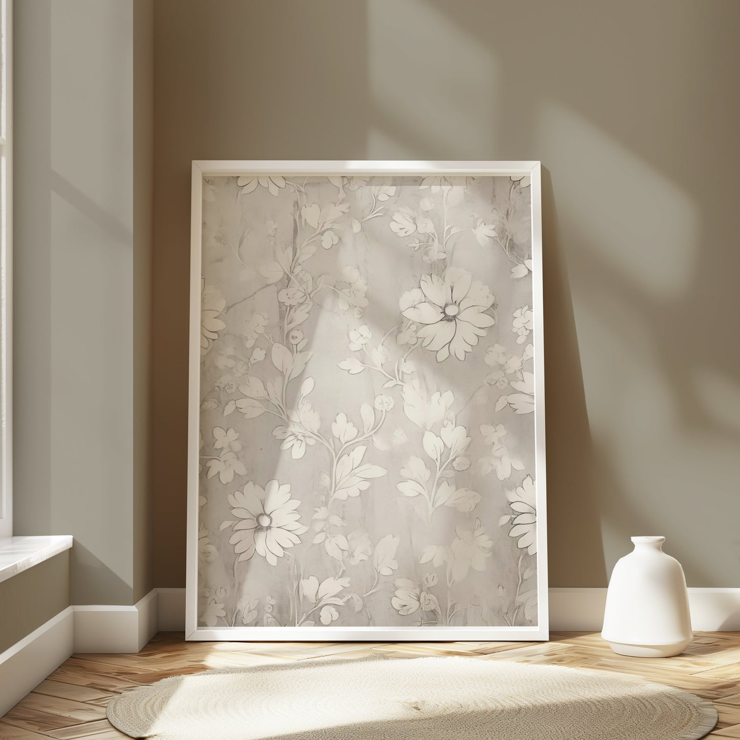 White floral art print in a white frame, leaning against a wall in a softly lit room with minimalist decor and natural tones.