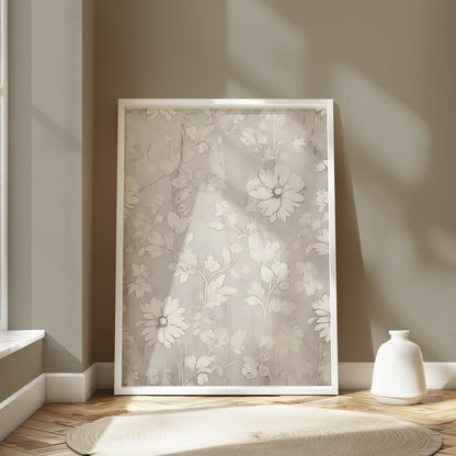 White floral art print in a white frame, leaning against a wall in a softly lit room with minimalist decor and natural tones.