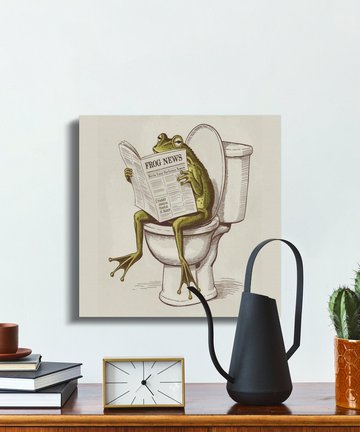 Novelty canvas wrap featuring a frog reading a newspaper on a toilet, styled on a desk for humorous home accents.