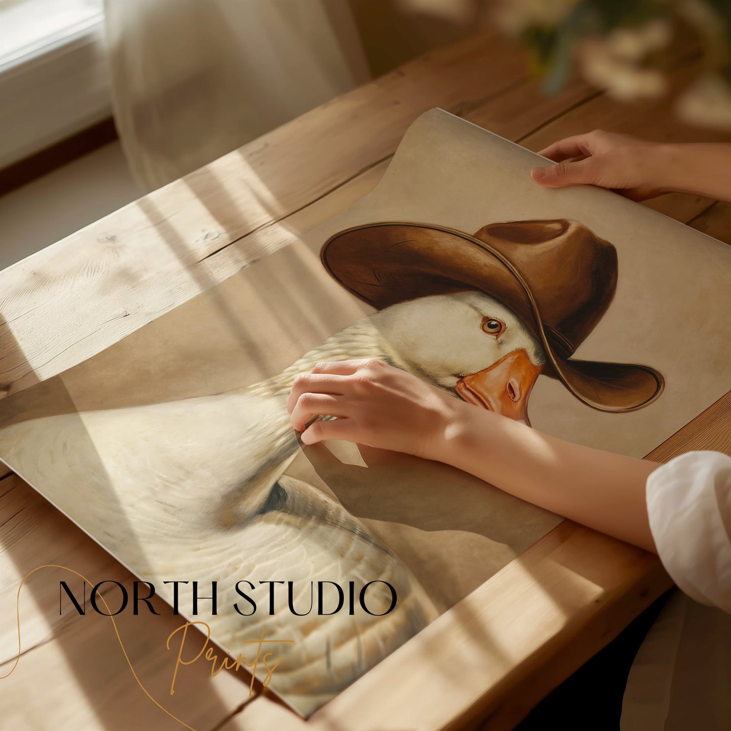 Hands holding a goose wearing cowboy hat art print on a wooden table, showcasing the premium quality and detailed illustration.