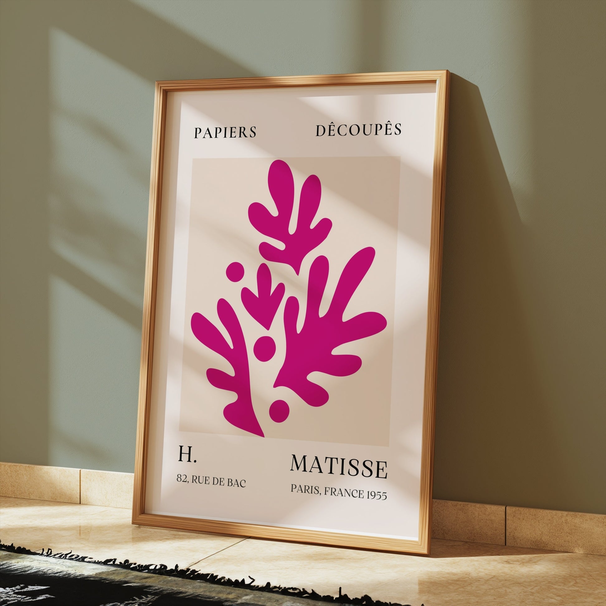 Henri Matisse Paris France 1955 Papiers Découpés poster in a wooden frame leaning against a green wall, illuminated by sunlight on a tiled floor.