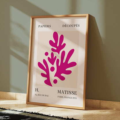 Henri Matisse Paris France 1955 Papiers Découpés poster in a wooden frame leaning against a green wall, illuminated by sunlight on a tiled floor.