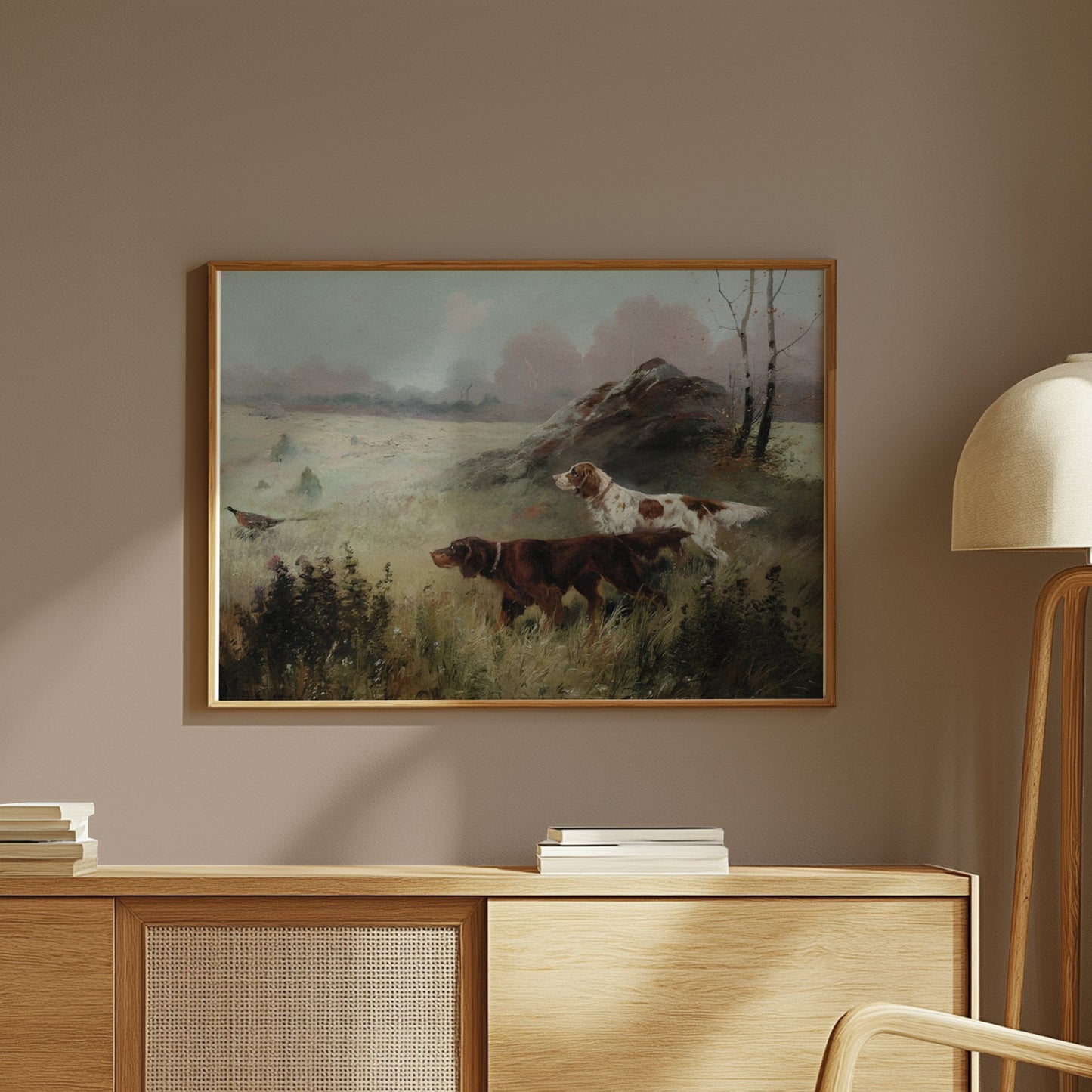 Framed hunting dogs in misty forest landscape art print displayed on a wooden cabinet in a modern interior.