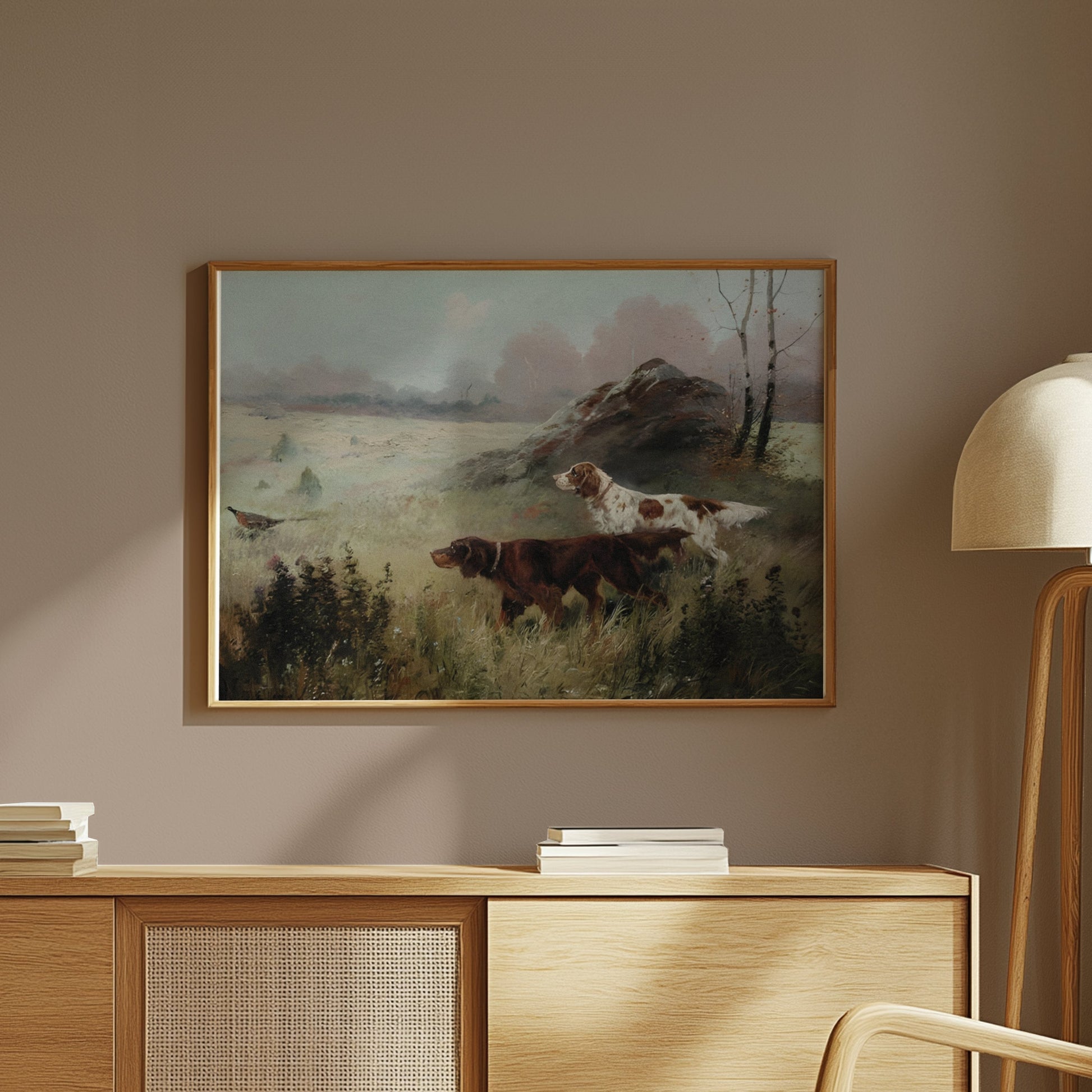 Framed hunting dogs in misty forest landscape art print displayed on a wooden cabinet in a modern interior.
