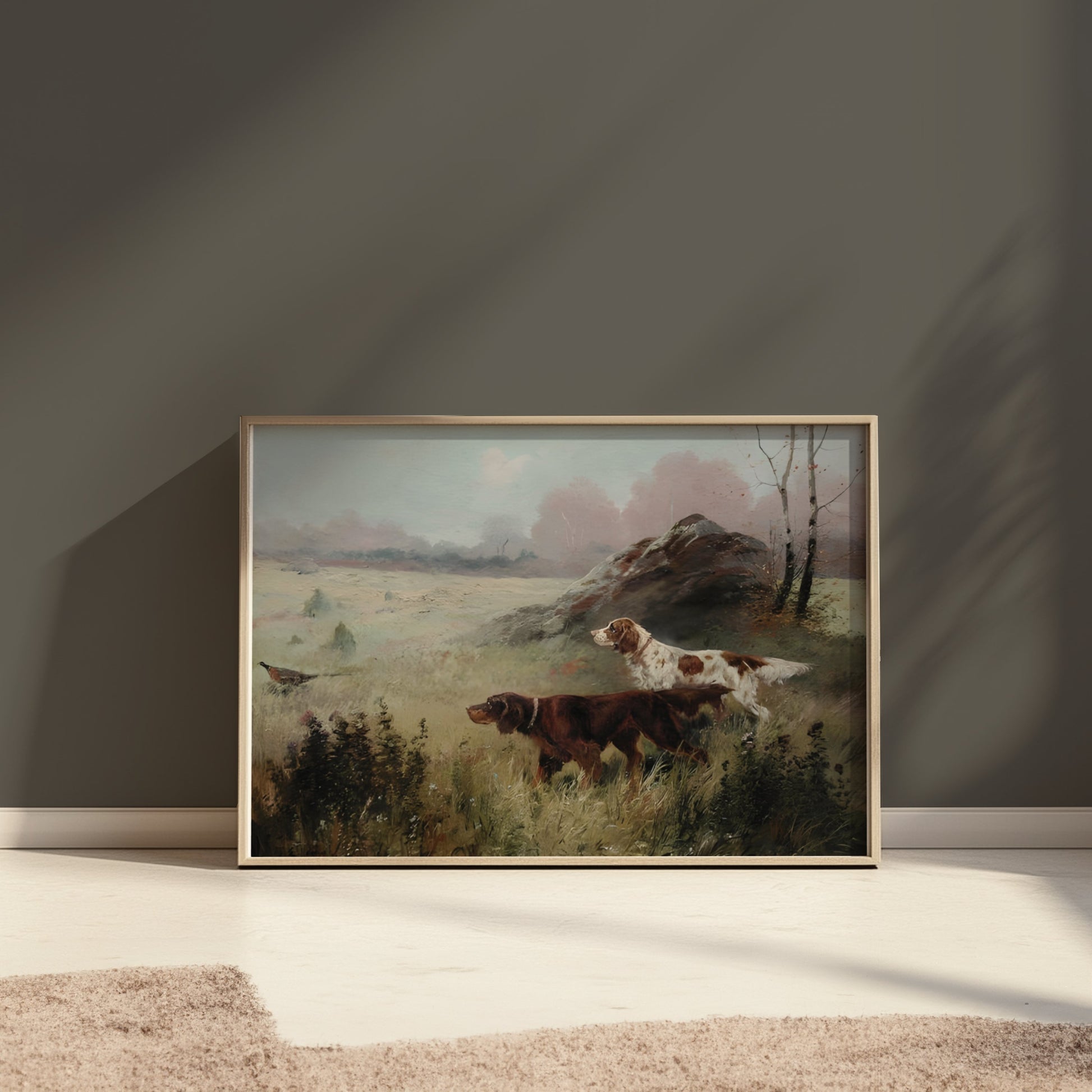 Framed hunting dogs in misty forest landscape poster placed on the floor against a dark wall with soft lighting.