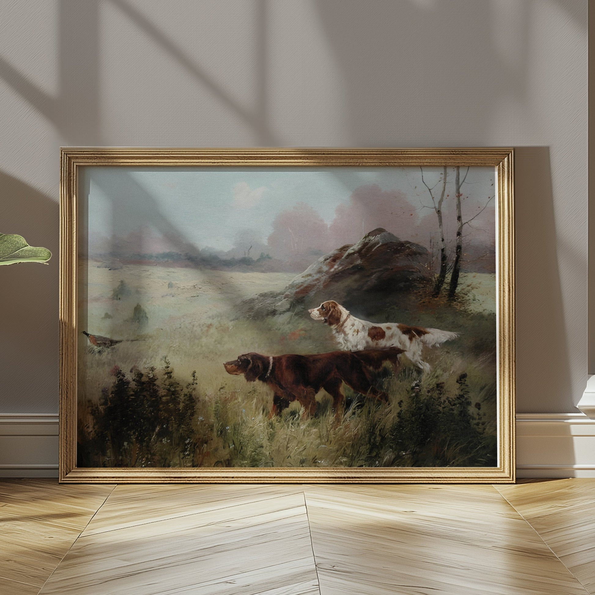 Hunting dogs in misty forest landscape art print in a gold frame, leaning on a wooden floor in a softly lit room.