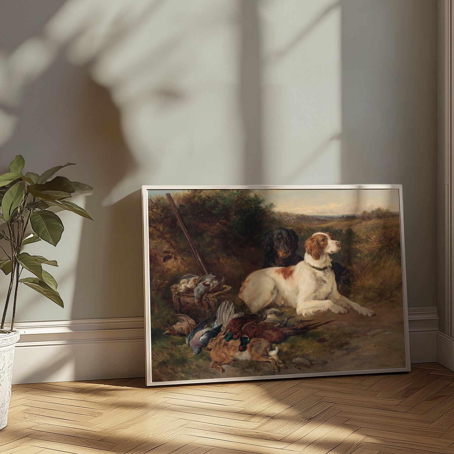 Hunting dogs and game birds artwork in a white frame, placed on a wooden floor with sunlight streaming through a nearby window.