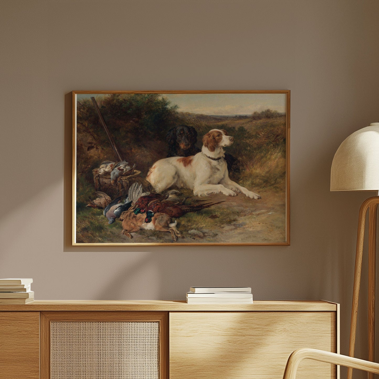 Framed hunting scene artwork featuring dogs and game birds, styled on a wooden desk in a warm-toned, rustic interior.
