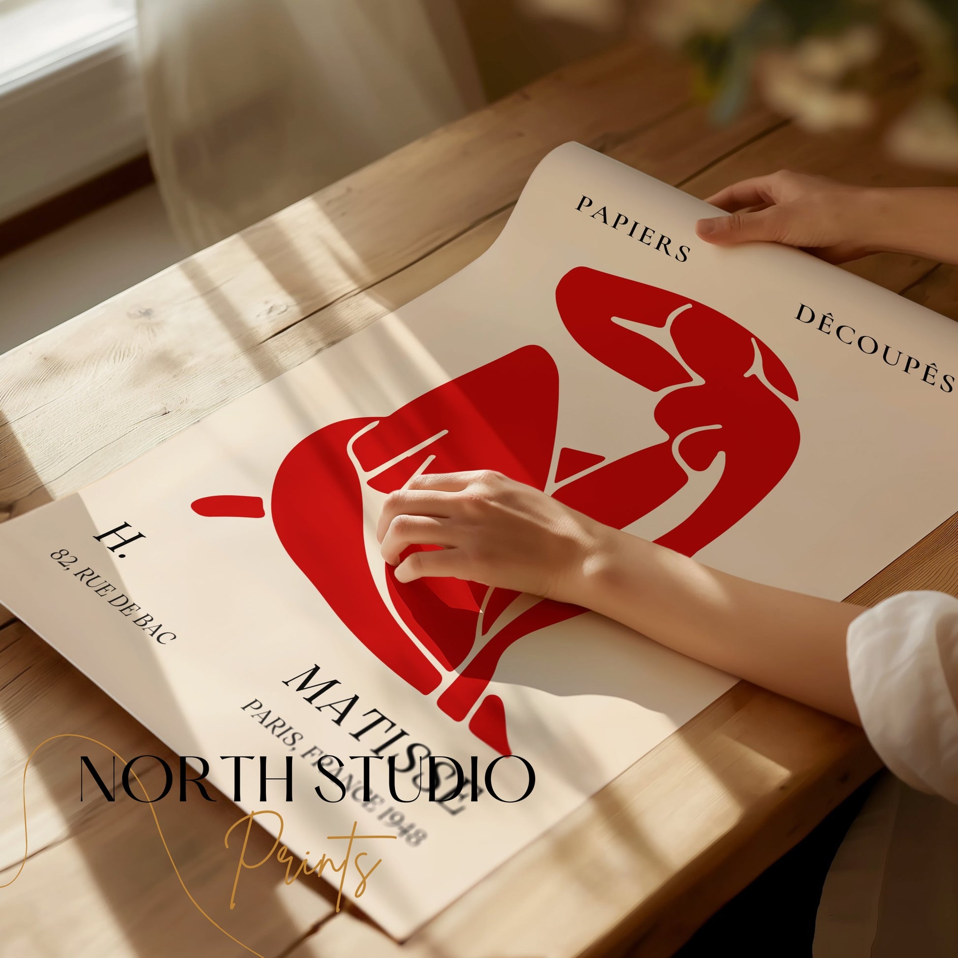 Close-up of H. Matisse 1948 Papiers Découpés art poster being unrolled on a wooden table, highlighting its vibrant red design and quality print.