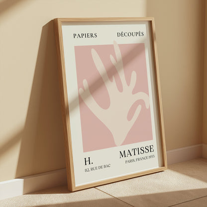Matisse Coral Hand Inspired Paris Art Poster in a wooden frame, displayed in a softly lit room with neutral walls for minimalist decor.