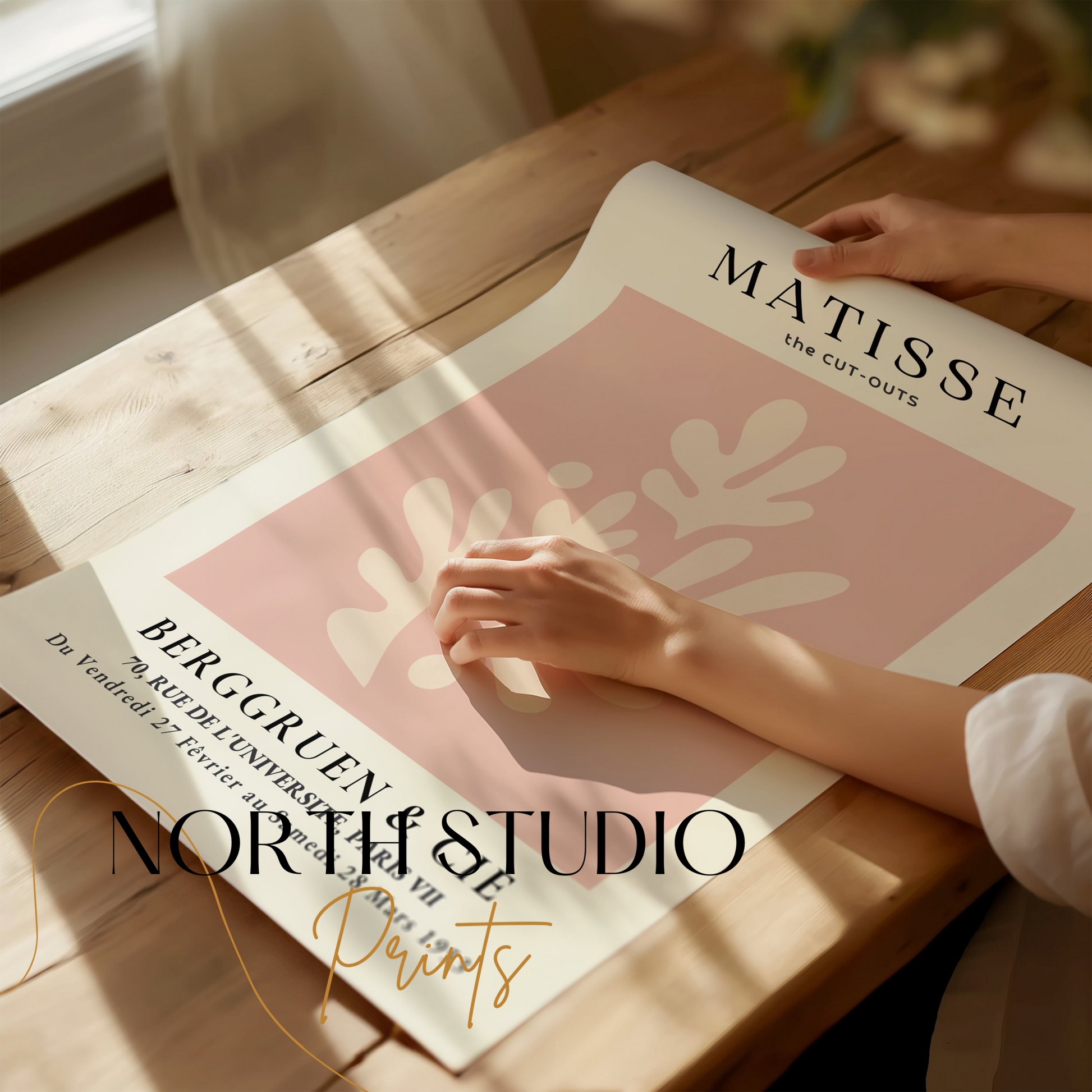 Hands unrolling a Matisse Cut-Outs Berggruen & Cie Paris VII poster on a wooden table, showcasing its elegant abstract design.