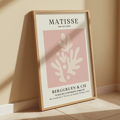Matisse Cut-Outs Berggruen & Cie Paris VII poster in a wooden frame, leaning against a wall in a softly lit beige room.