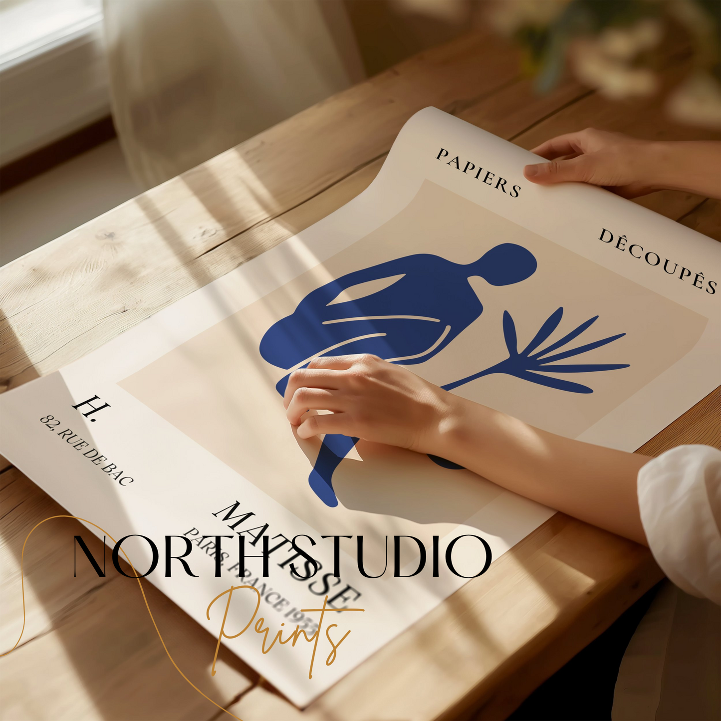 Unframed Matisse inspired modern art poster with a blue abstract figure, being unrolled on a wooden table with 'North Studio Prints' branding.