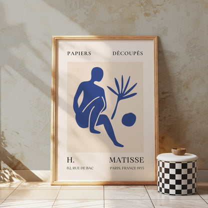 Matisse inspired art poster in a wooden frame, featuring a blue abstract figure, displayed against a textured wall with soft lighting.