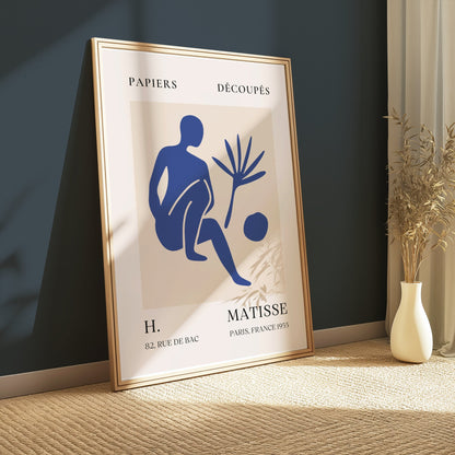 Framed Matisse inspired art poster with a blue abstract figure, leaning against a dark green wall, styled with a vase and natural light.