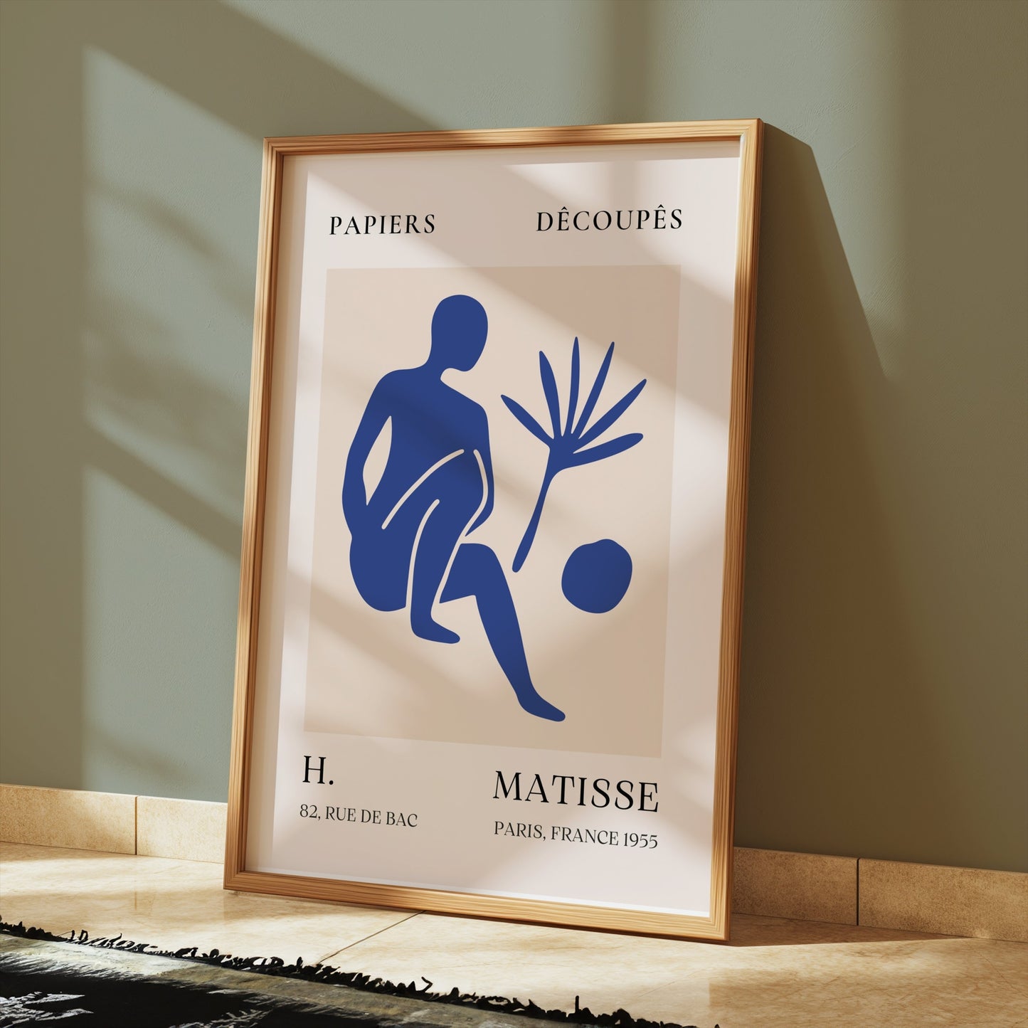 Matisse inspired modern art poster in a wooden frame, featuring a blue abstract figure, displayed on a tiled floor with soft shadows.