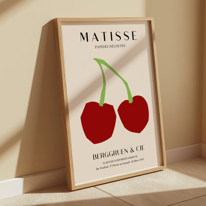 Framed Matisse Papiers Découpés art print poster with red cherry design, displayed leaning against a beige wall in natural sunlight.