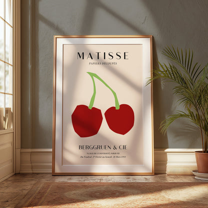 Matisse Papiers Découpés cherry art print poster in a wooden frame, displayed in a sunlit corner with plants and warm decor.