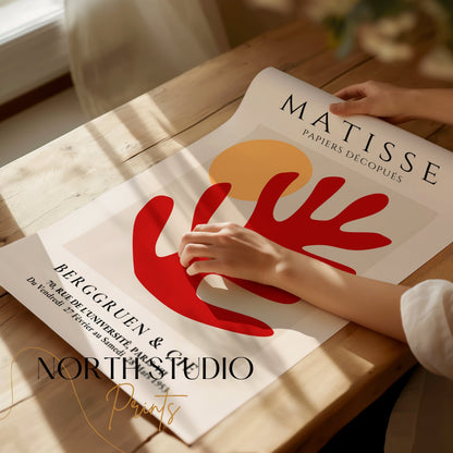 Unframed Matisse Art Poster with red coral and orange sun, being handled on a wooden table, showcasing its vibrant design and premium print quality.