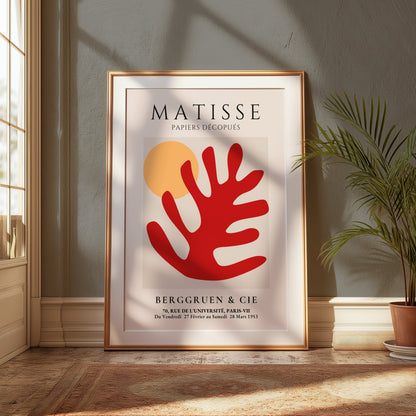 Large framed Matisse Art Poster featuring red coral and orange sun, leaning against a wall in a bright room with natural light and greenery.