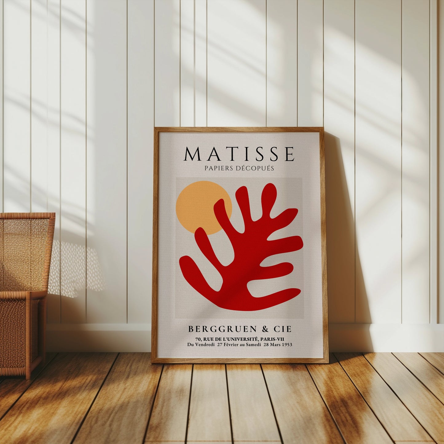 Matisse Art Poster with red coral and orange sun, framed and placed on a wooden floor in a sunlit room with white panel walls and wicker decor.