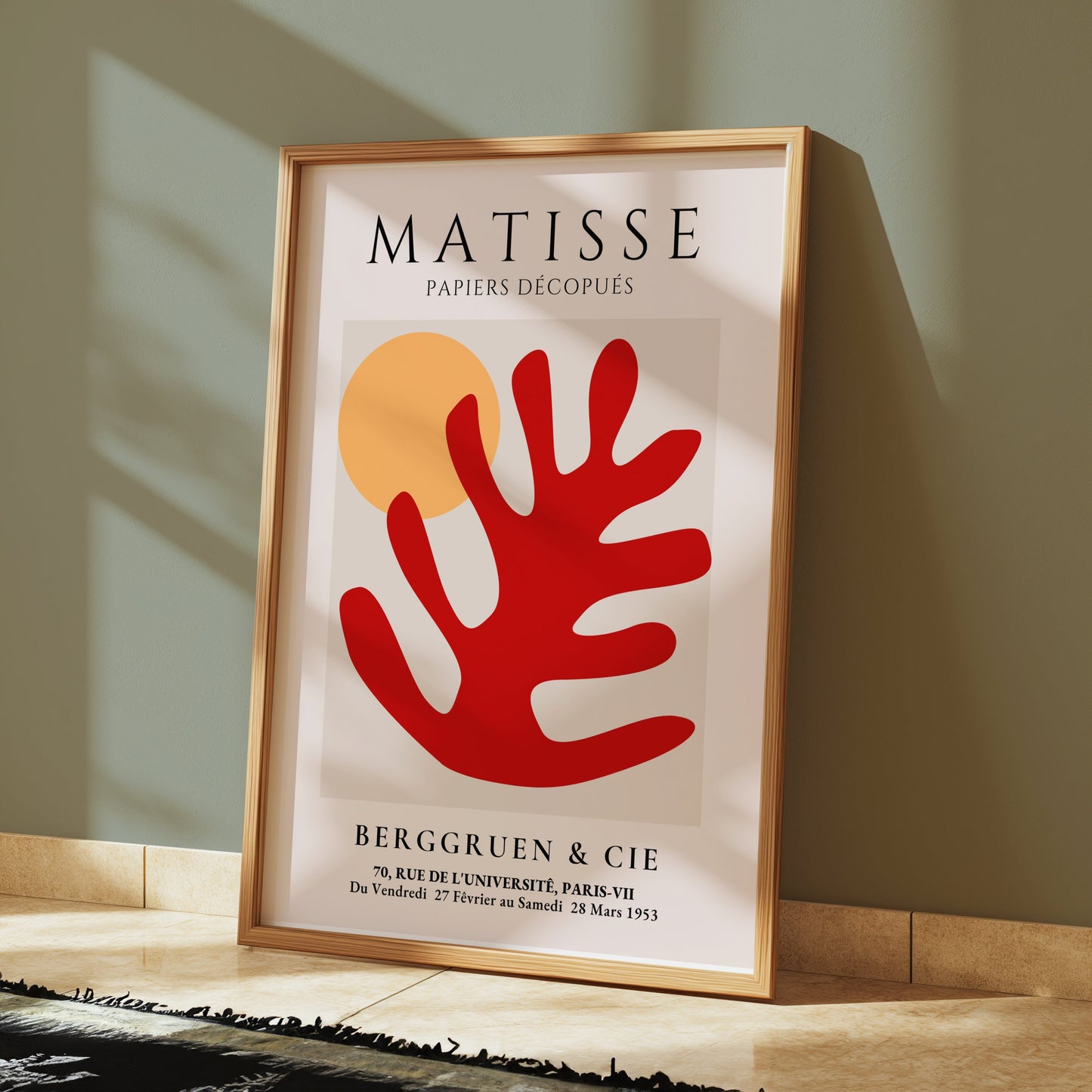 Framed Matisse Art Poster with red coral cut-out and orange sun, leaning against a green wall in a modern room with soft lighting and minimal decor.