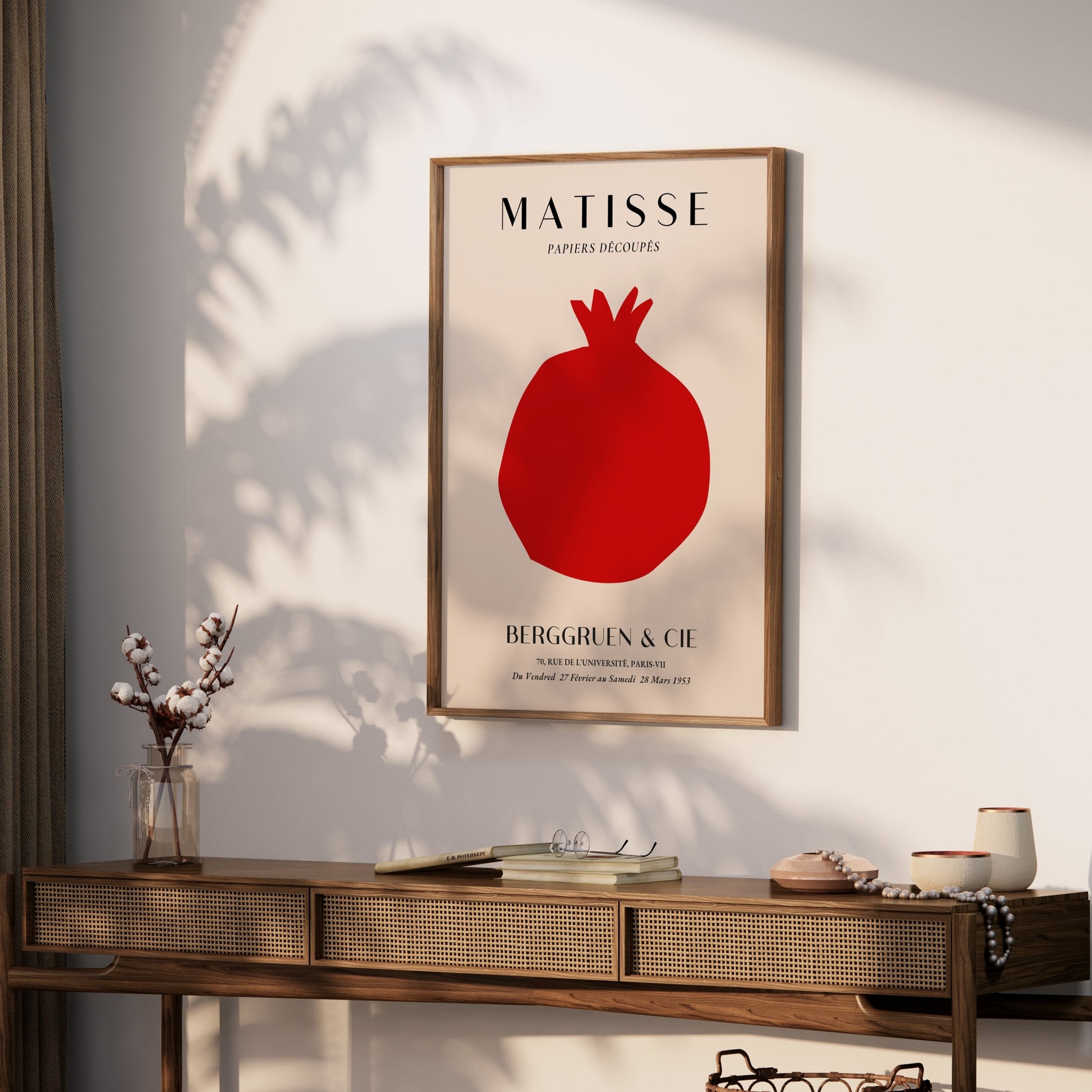 Framed Matisse Papiers Decoupes Berggruen & Cie poster with red pomegranate design displayed above a wooden console table in a sunlit room.
