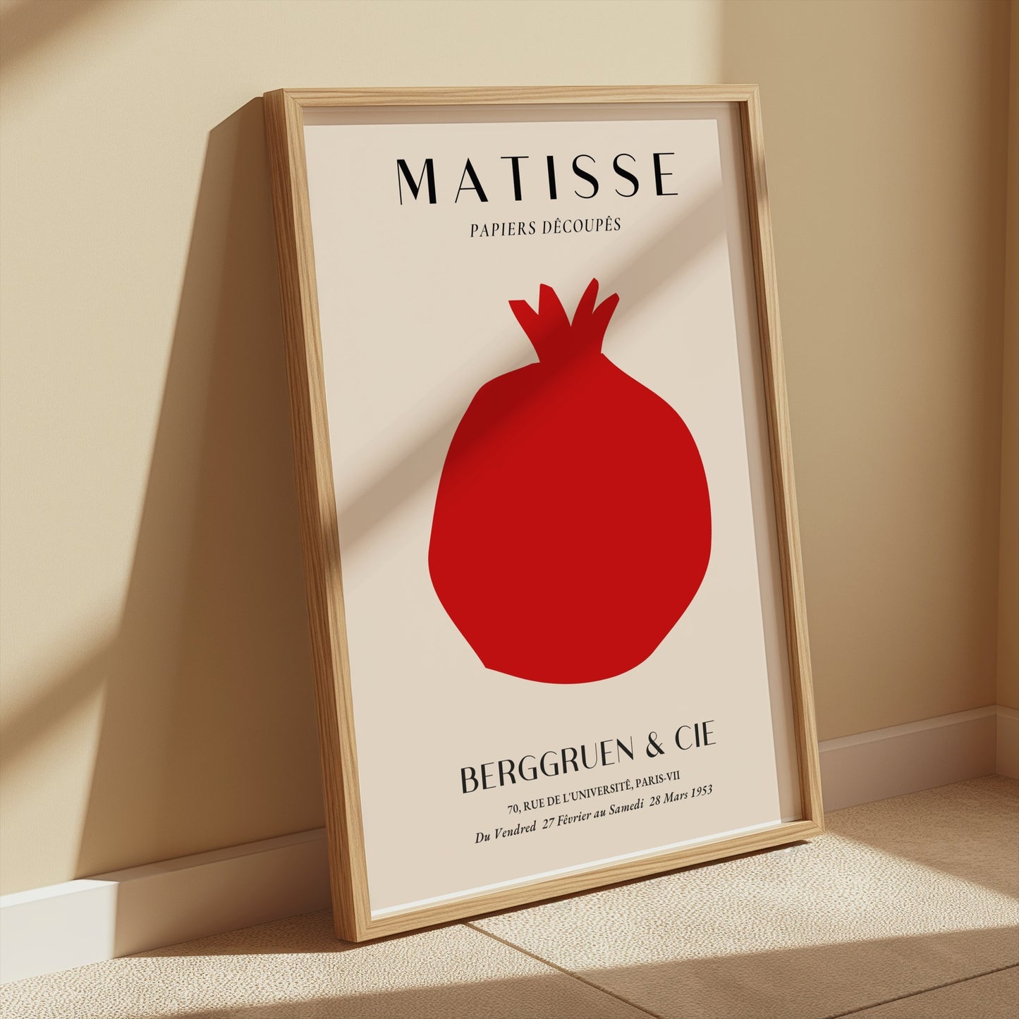 Matisse Papiers Decoupes Berggruen & Cie poster in a wooden frame leaning against a beige wall with soft sunlight illuminating the area.