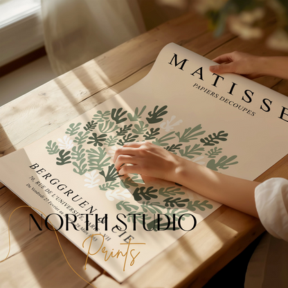 Hands unrolling a Matisse Papiers Decoupes poster on a wooden table, showcasing its green botanical cut paper art and vintage design.