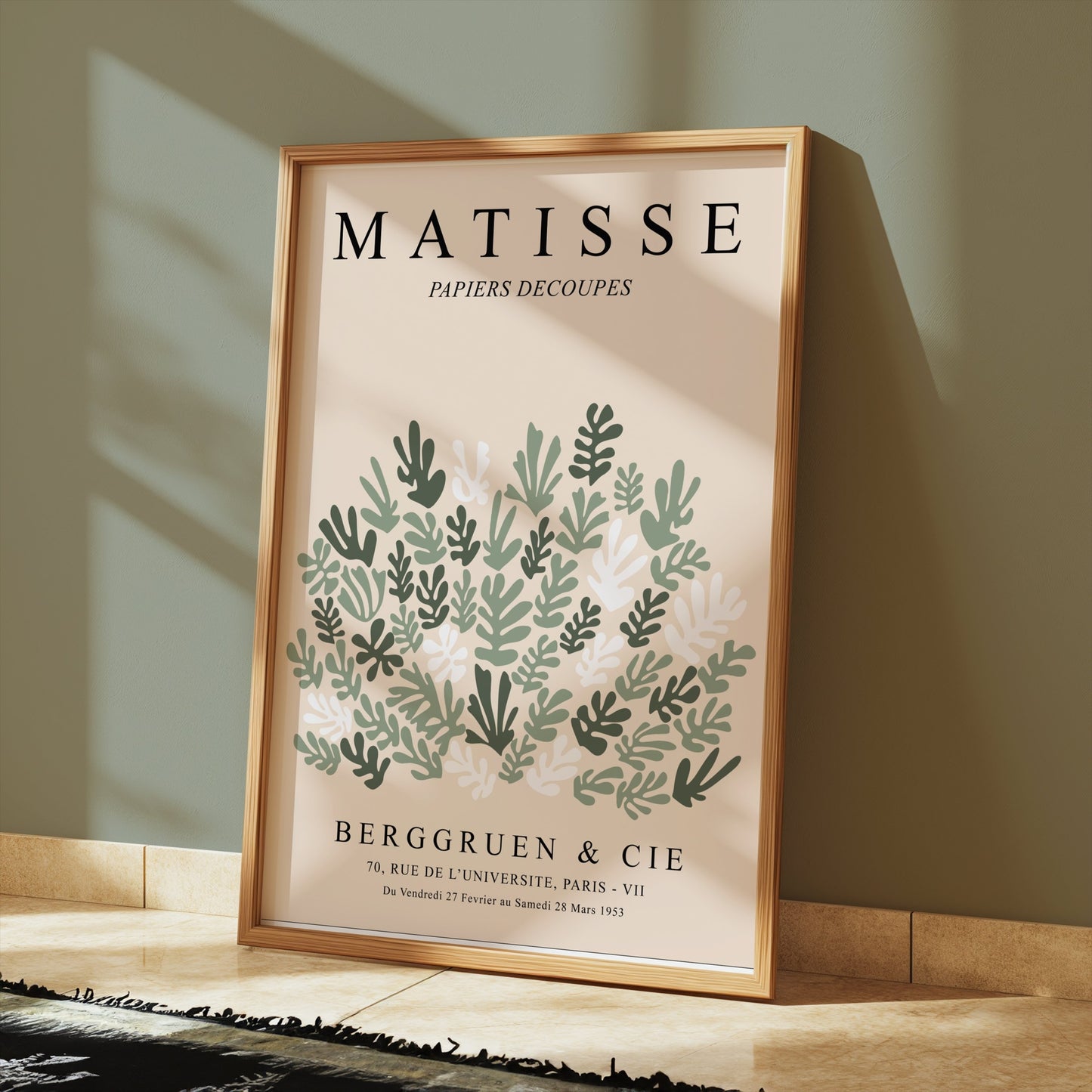 Matisse Papiers Decoupes poster in a wooden frame, styled on a floor against a green wall with sunlight highlighting its botanical design.