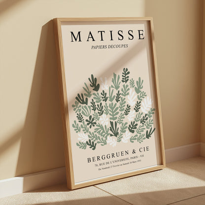 Matisse Papiers Decoupes poster in a wooden frame, leaning against a beige wall with sunlight casting soft shadows for a cozy look.