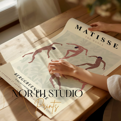 Hands unrolling a Matisse The Dance exhibition poster on a wooden table, showcasing the vibrant design and Berggruen & Cie details.